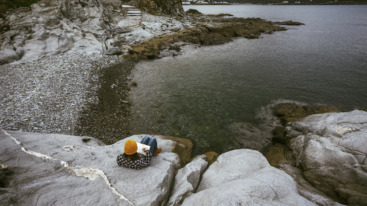 Young woman reading a book on the rock at seashore.