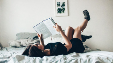 Dame die op bed ligt en een boek over feminisme leest