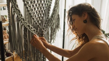 Dame die bezig is met een wandkleed maken door middel van macramé