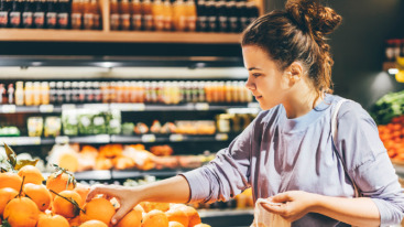 Woman choosing orange at market and using reusable eco bag.
