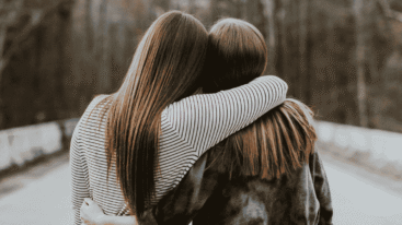 Twee vrouwen omhelzen elkaar met gezichten in tegengestelde richting.