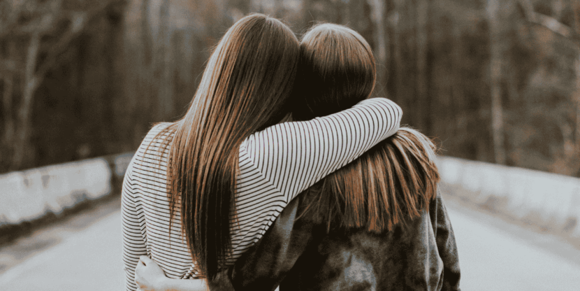 Twee vrouwen omhelzen elkaar met gezichten in tegengestelde richting.