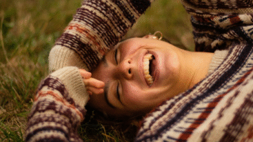 vrouw ligt in het gras en lacht naar de camera
