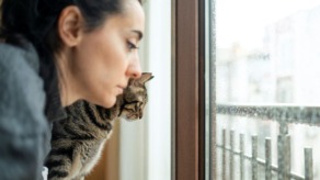 vrouw kijkt met kat somber door slecht weer naar buiten