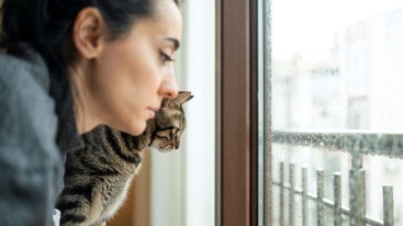 vrouw kijkt met kat somber door slecht weer naar buiten