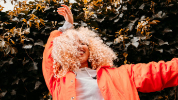 Een blije zelfverzekerde vrouw met een oranje jas en krullend haar