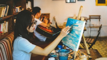 Dame in een atelier die een landschap aan het schilderen is.