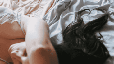 Peinzend brunette meisje met haar dat een hart vormt, liggend op het bed.